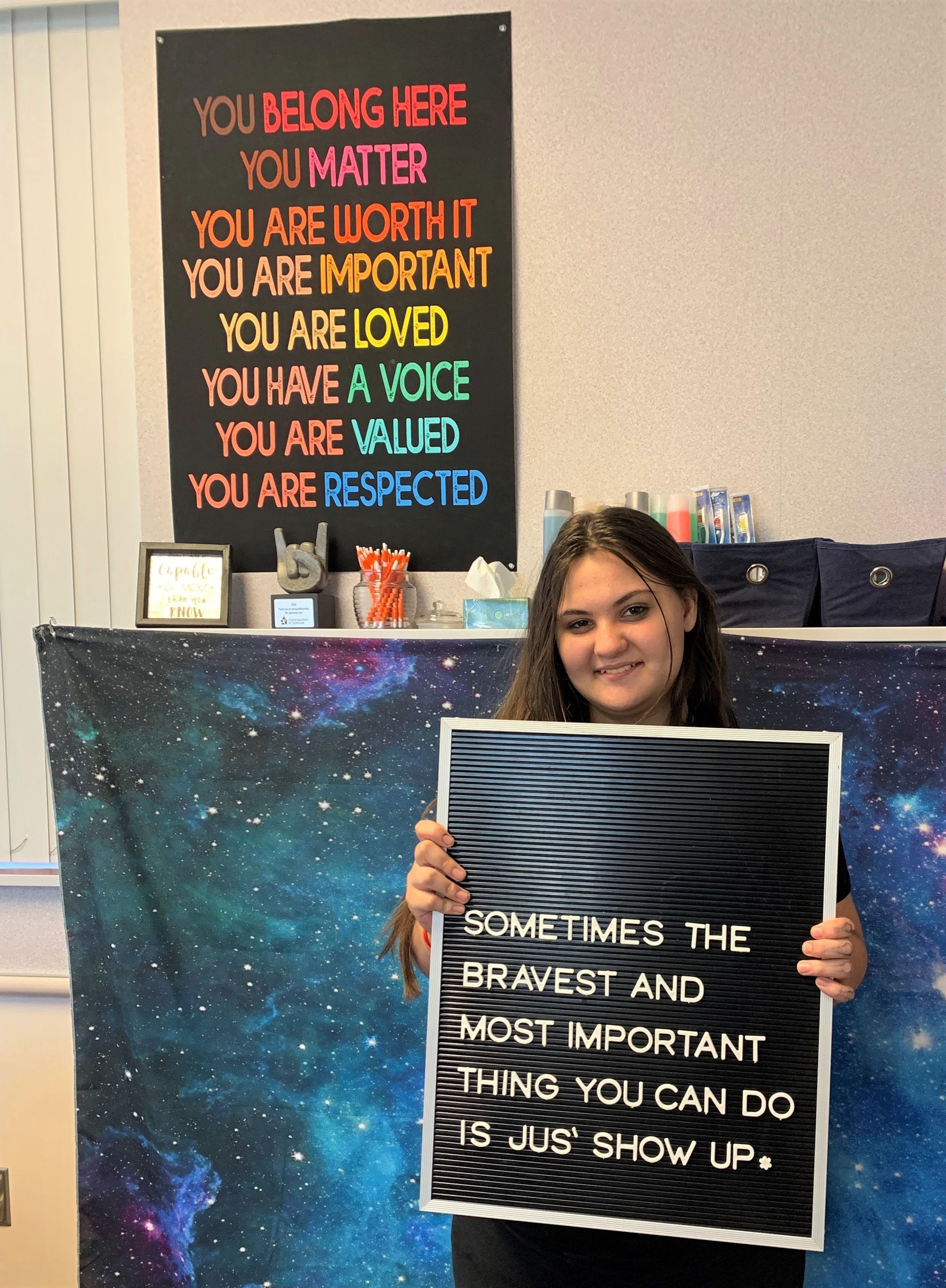 Poster reads: You belong here, you matter, you are worth it, you are important, you are loved, you have a voice, you are valued, you are respected . Student holds a sign that says: Sometimes the bravest and most important thing you can do is just show up.e.