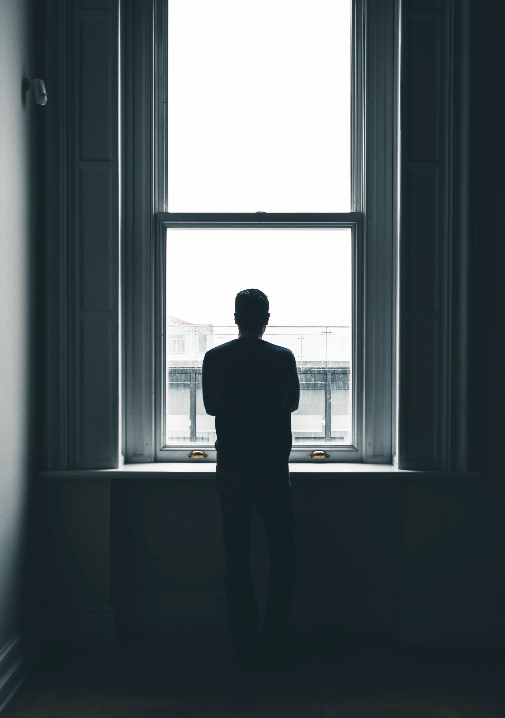 Photo of a person silhouetted in a dark room looking out the window