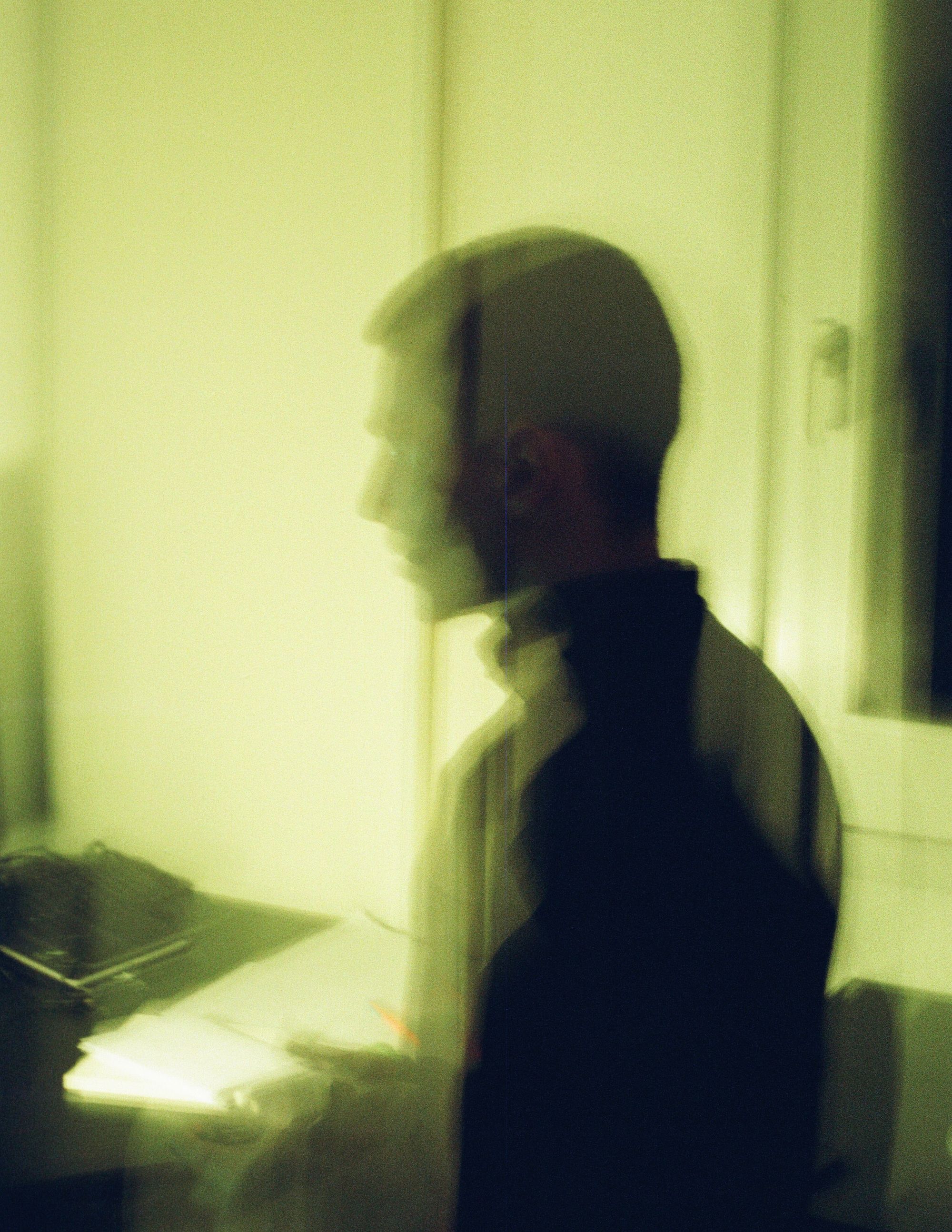 Black and green image of a man at a desk; image is double exposed, foggy, and dreamlike