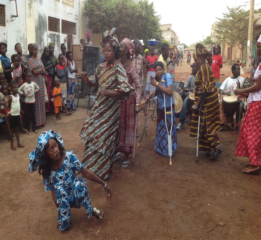 A few women, some on crutches, with a crowd, including men with drums