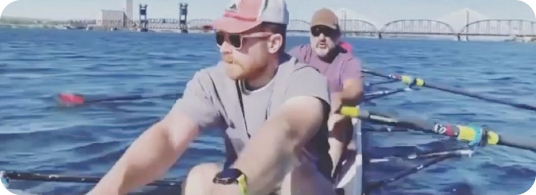 Image of rowers in a boat with the train bridge behind them