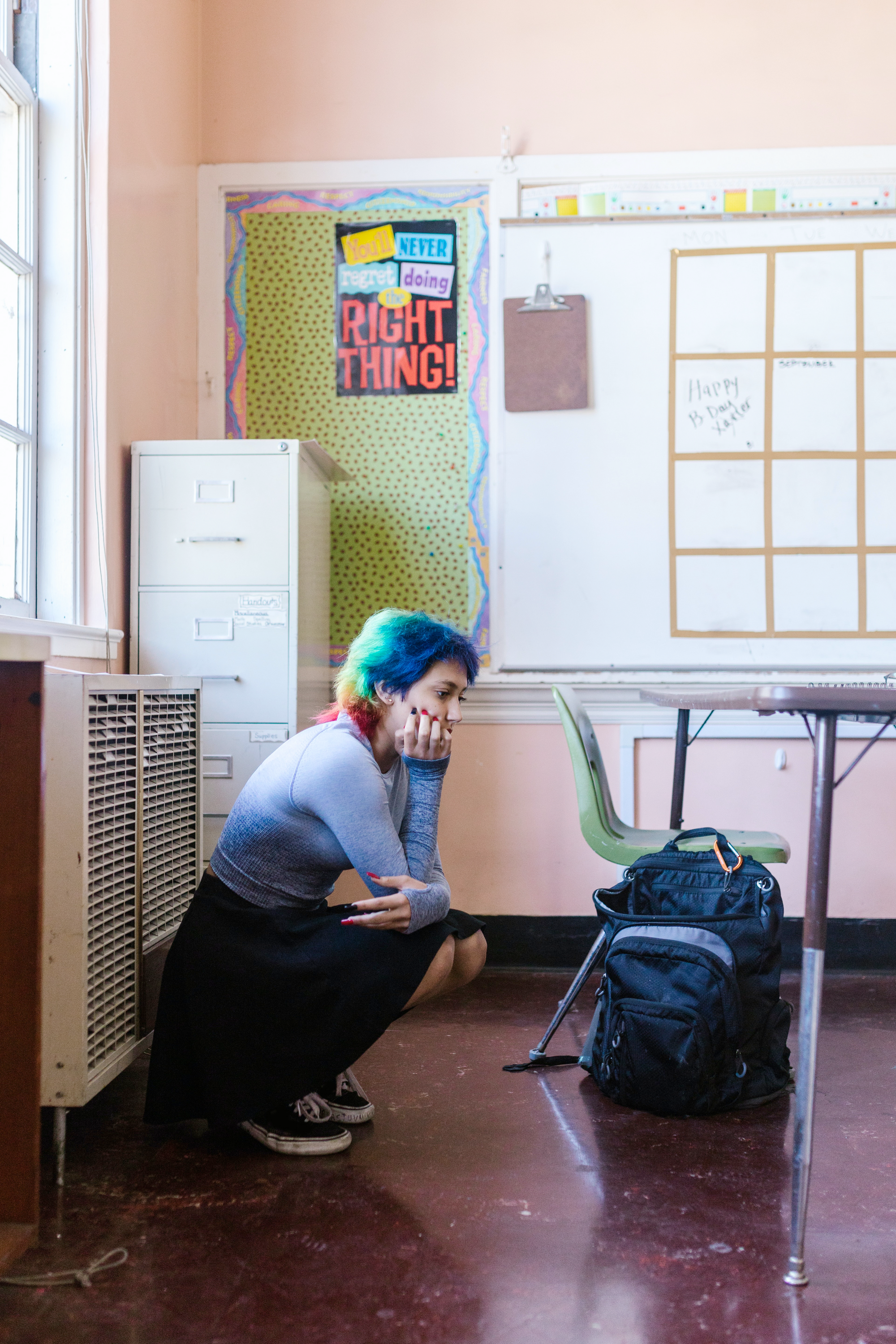 Image of a student with rainbow hair crouched down on the ground in a classroom