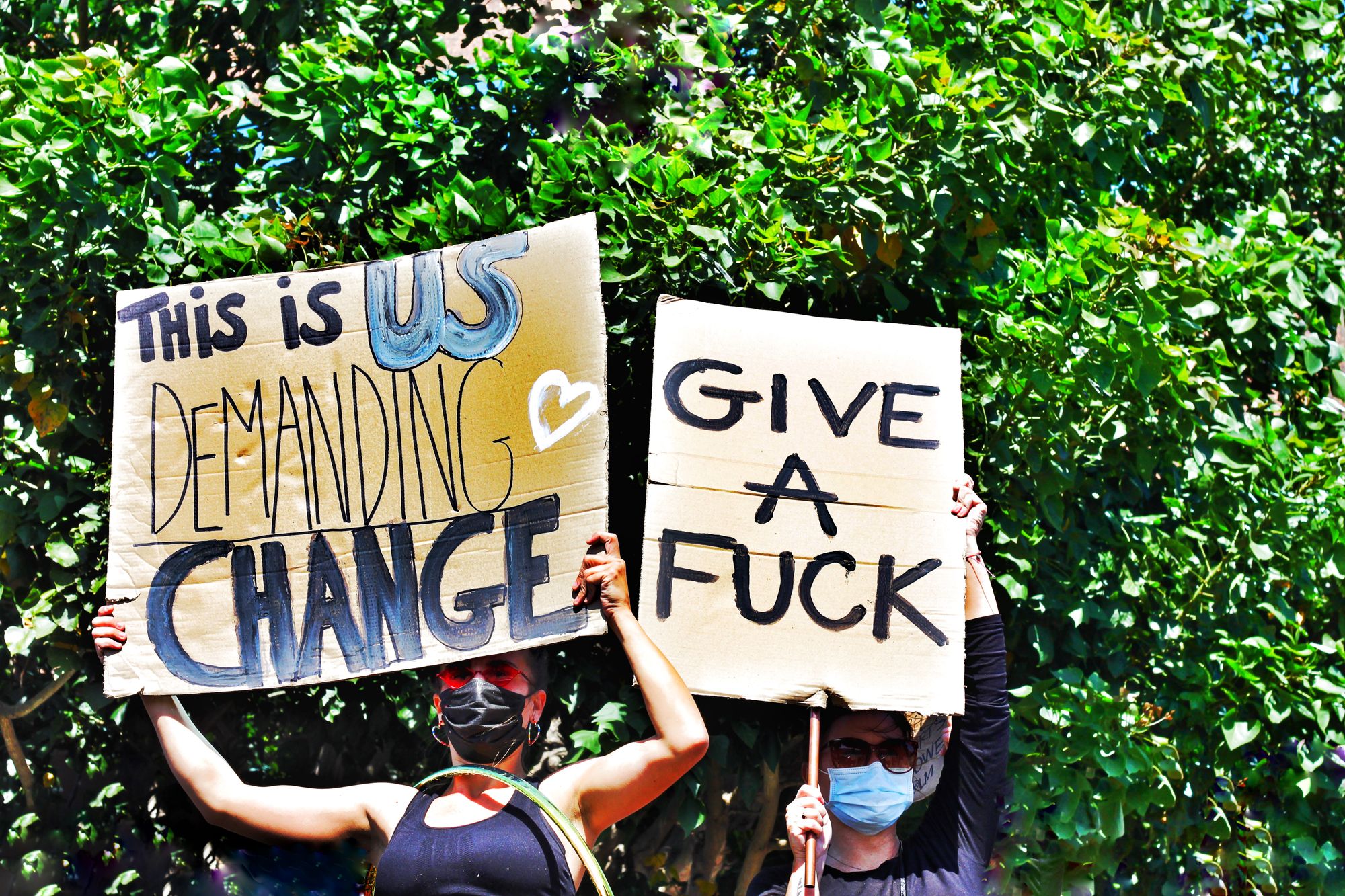 Two activists holding signs that say "This is us demanding change: and "give a fuck"