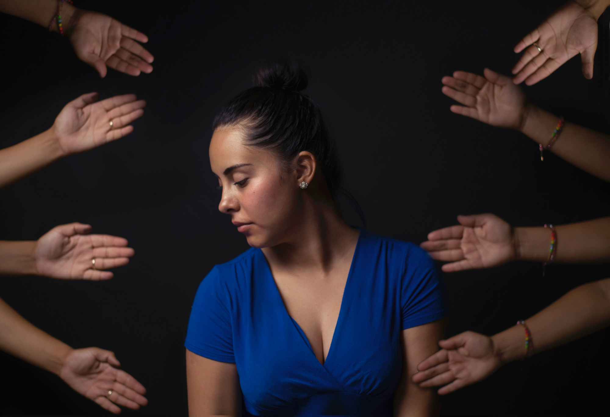 Photo of a young woman sitting, ignoring many hands reaching toward her