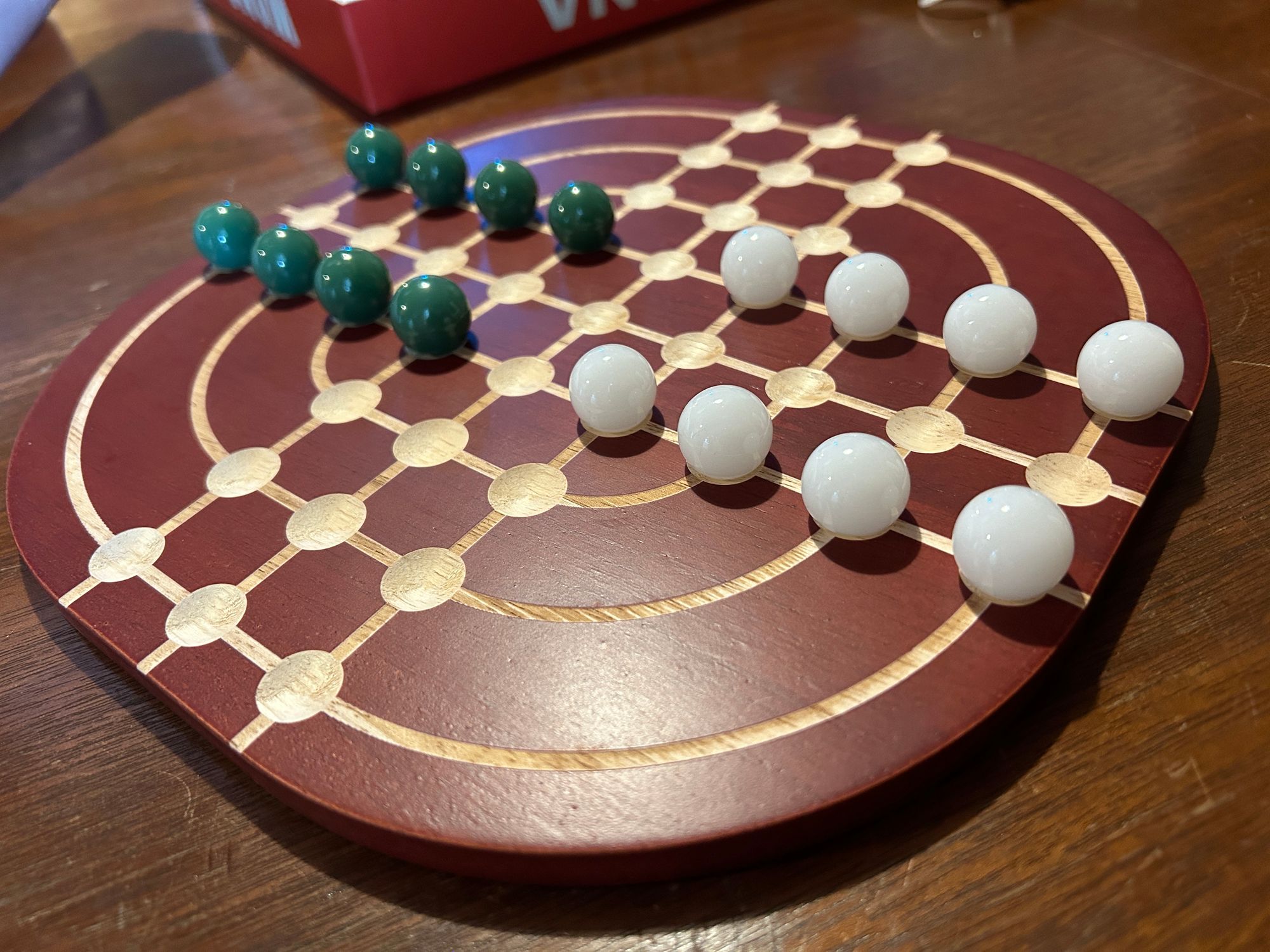 An image of a wooden board game with spherical pieces places in divots on the board.