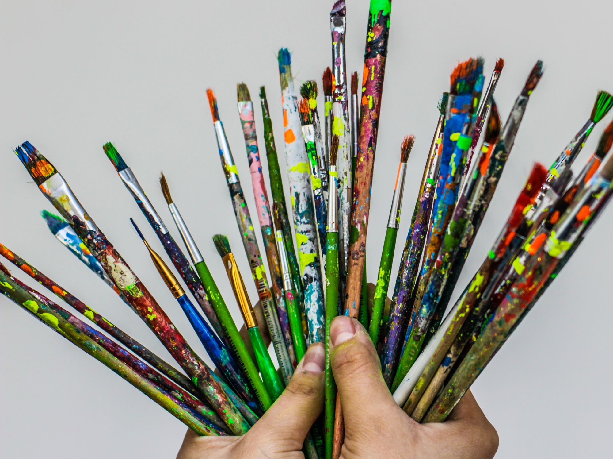 An image of a person holding a lot of used paintbrushes in their hands.