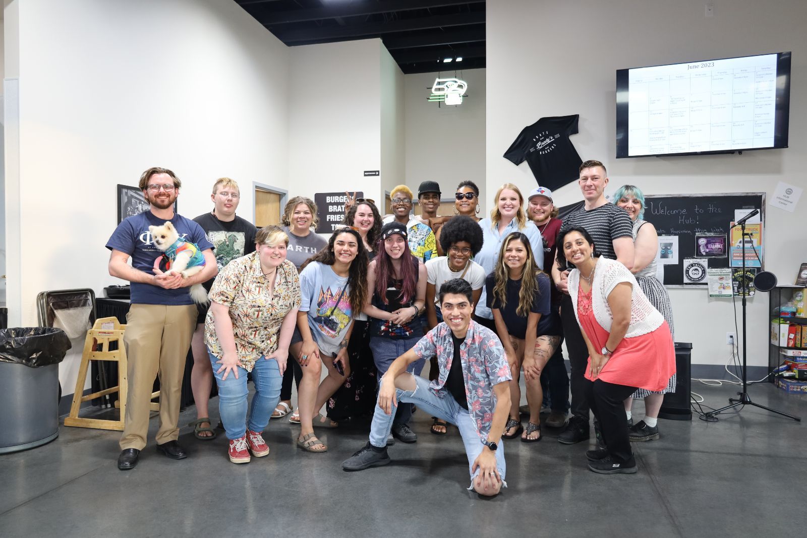 An image of people standing together in a group posing for a picture, a person on the left is holding a small dog.