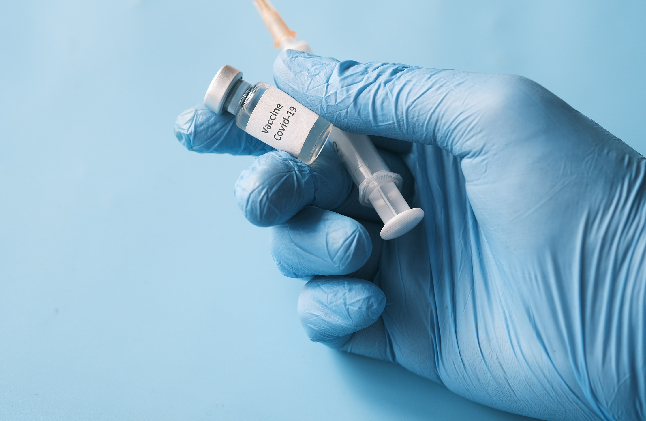 An image of a person holding a syringe and a vial of medicine labeled "Vaccine Covid-19"